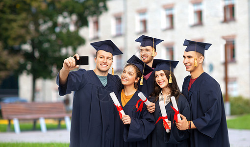 教育,毕业人的群快乐的研究生砂浆板学士学位礼服与文凭采取自拍智能手机校园建筑背景毕业证书的毕业生用手机自拍背景图片