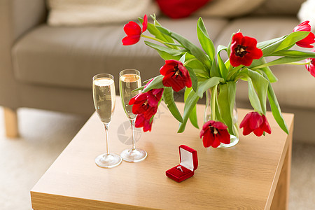 情人节浪漫的钻石戒指红色天鹅绒礼品盒,香槟杯鲜花桌子上钻石戒指,香槟鲜花桌子上图片
