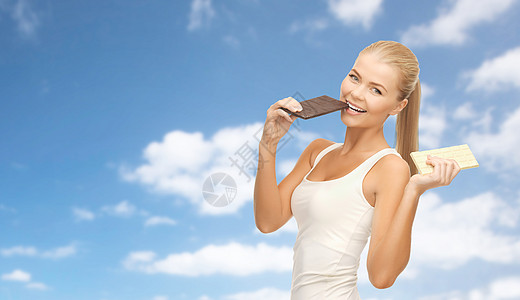 减肥饮食快乐的女人吃黑巧克力,而白色的蓝天云背景快乐的女人吃黑巧克力而白色图片