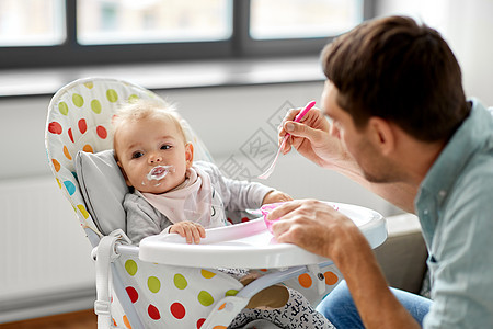 家庭,食物,饮食人的父亲喂养小婴儿女儿坐高椅子上,用勺子家里父亲家高椅子上喂婴儿图片