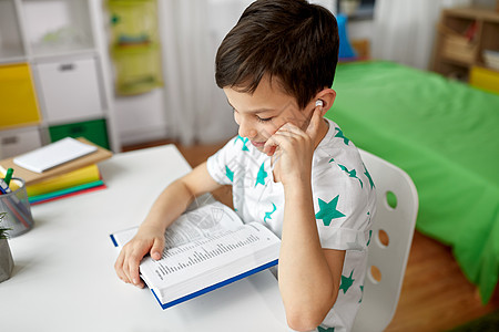 教育,童技术快乐的学生男孩耳机阅读书籍学外语家里学生男孩戴着耳机家看书图片