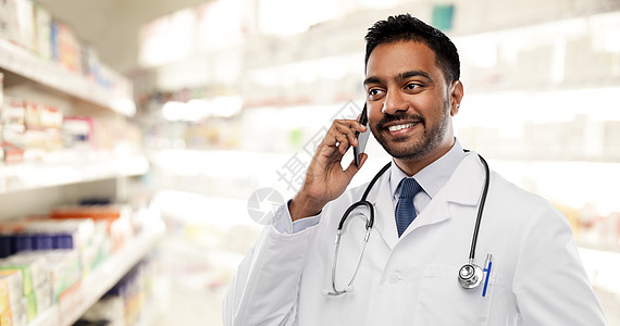 医学,技术医疗微笑的印度男医生药剂师穿着白色外套,听诊器呼叫智能手机药店背景微笑的印度男医生打电话给智能手机图片