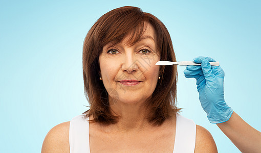 美容,整形手术美容老年女子外科医生手与手术刀的蓝色背景老年女子外科医生用手术刀图片