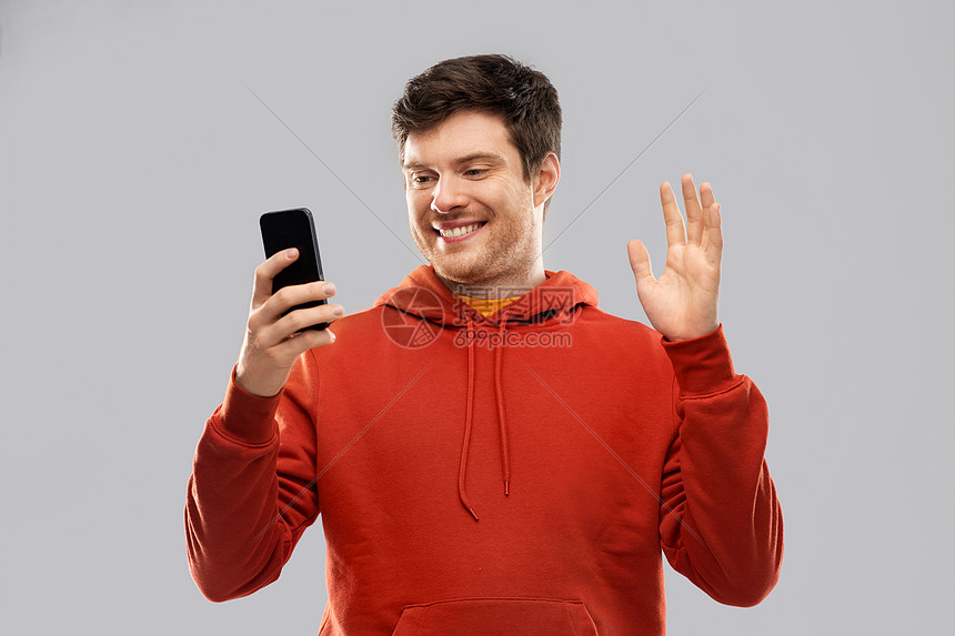 技术,沟通人的微笑的轻人穿着红色帽衫,智能手机自拍灰色背景上进行视频通话男人用智能手机自拍视频通话图片