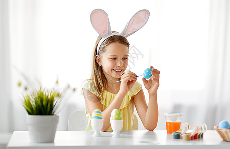 复活节,假日人们的快乐的女孩戴着兔子耳朵,头带着色鸡蛋与颜色刷子家里快乐的女孩家里给复活节彩蛋着色背景图片