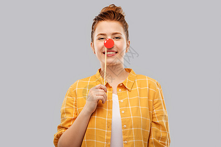 红鼻子日,派照片展位的微笑的红头发少女穿着格子衬衫,灰色背景上小丑鼻子微笑的红发少女,着小丑的鼻子图片