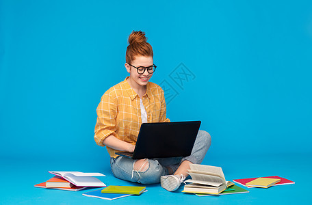 教育,高中,技术人的红色头发十几岁的学生女孩穿着格子衬衫撕裂牛仔裤与书籍用笔记本电脑明亮的蓝色背景红头发的十几图片