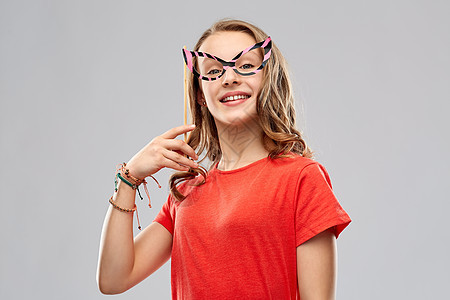 派道具,照片亭人们的微笑的十几岁女孩穿着红色T恤,灰色背景上戴着滑稽的眼镜带着派眼镜的微笑的十几岁女孩图片