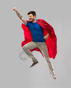 超级力量人的快乐的轻人红色超级英雄斗篷空中飞行的灰色背景穿着红色超级英雄斗篷的人空中飞行图片