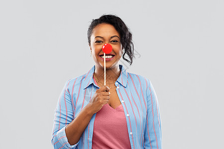 红鼻子日,派道具照片展位快乐的非裔美国轻妇女与小丑鼻子灰色背景快乐的非裔美国女人,红色小丑鼻子图片