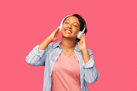 人,技术音频设备的快乐的非裔美国轻妇女耳机听音乐的粉红色背景非洲女人戴着耳机听音乐图片