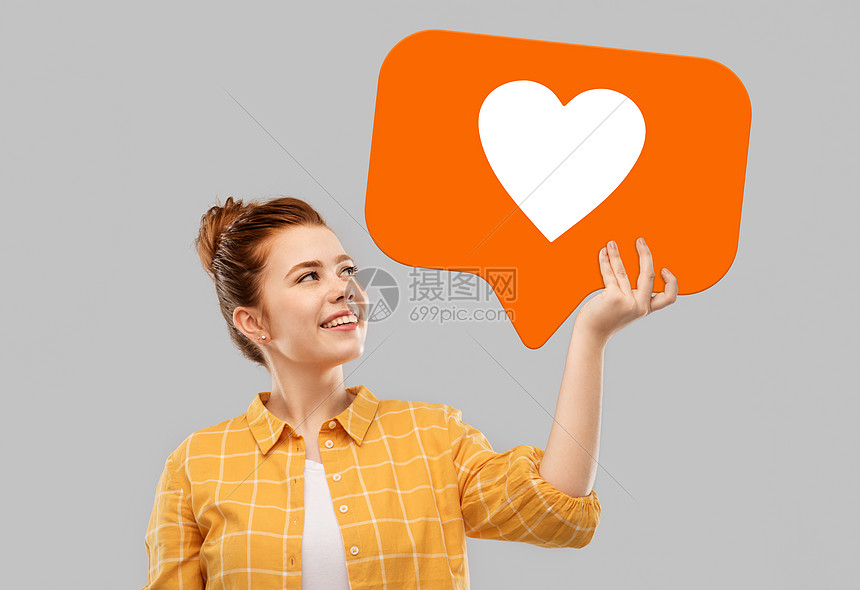 社交媒体营销,互联网人的微笑的红头发少女穿着格子衬衫,灰色背景上着心脏图标红头发的十几岁女孩着演讲泡泡图片
