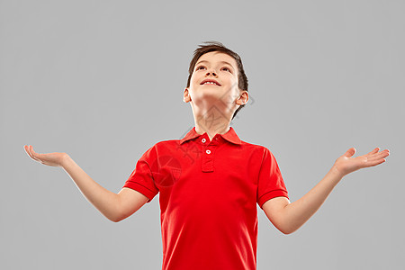 童,优雅祝福的快乐的感恩小男孩穿着红色马球T恤,仰望灰色的背景快乐的感恩男孩穿着红色T恤抬头看图片
