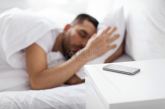 熟睡的男人靠近床头柜上的智能手机图片