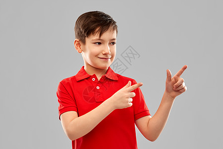 童,想法人的快乐的小男孩穿着红色马球T恤,手指灰色的背景下穿着红色T恤的快乐男孩指着边图片