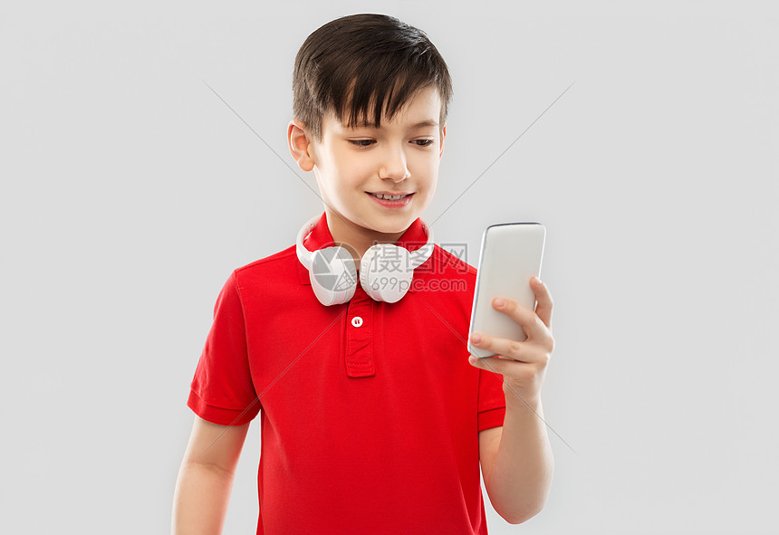 技术,童人的微笑的小男孩穿着红色马球T恤,戴着耳机脖子上用智能手机灰色背景带耳机智能手机的红色T恤男孩图片