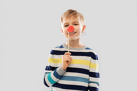 红鼻子日,照片亭童的微笑的小男孩与小丑鼻子灰色的背景带着红色小丑鼻子派道具的微笑男孩图片