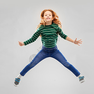童,时尚人的微笑的红色头发女孩穿着绿色条纹衬衫牛仔裤跳过灰色背景微笑的红头发女孩穿着条纹衬衫跳跃图片