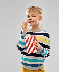 快餐,垃圾食品童的小男孩穿条纹套头衫吃爆米花纸桶灰色背景小男孩纸桶里吃爆米花图片
