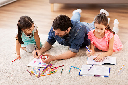 家庭父亲休闲的父亲花时间他的小女儿素描簿上用蜡笔画画,躺家里的地板上父亲带着小女儿家画画图片