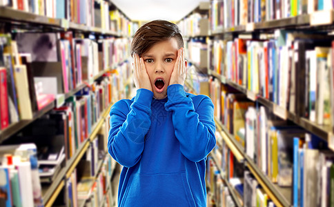 童,表情人的震惊害怕的男孩触摸他的脸书架上的图书馆背景图书馆书架上吓坏了的男孩图片