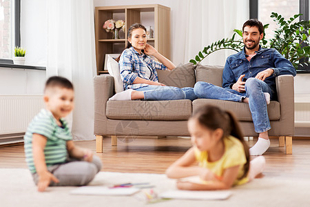 家庭休闲人的快乐的母亲父亲坐沙发上,看着孩子家画画幸福的家庭家里度过空闲时间图片