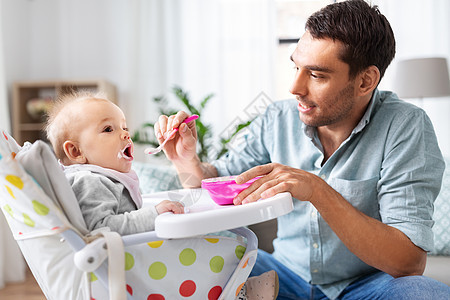 家庭,食物,饮食人的快乐的父亲喂养小婴儿女儿坐高椅子上,用勺子家里父亲家高椅子上喂快乐的婴儿图片