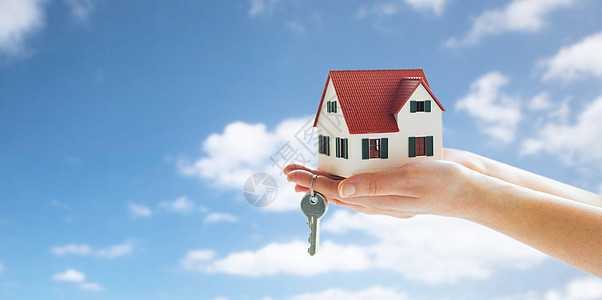 抵押贷款,房地产财产近距离的手着房子模型家庭钥匙蓝天云彩的背景双手紧握房屋模型钥匙图片