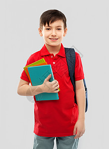 学校,教育人的微笑的小学生男孩穿着红色马球T恤,戴着眼镜,带着书灰色背景的袋子带着书书包微笑的小学生图片