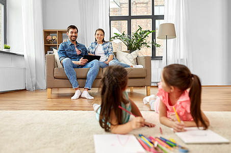 家庭休闲人的快乐的母亲父亲坐沙发上,看着女儿家画画幸福的家庭家里度过空闲时间图片