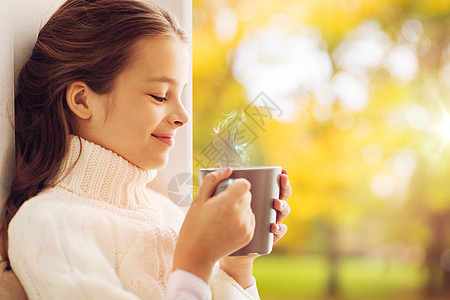 童季节的美丽的女孩与茶杯毛衣坐家里的窗户秋天的背景秋天,带着茶杯的女孩坐家里的窗户上图片