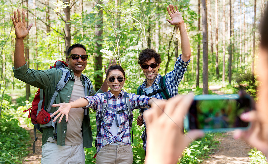 旅行,旅游徒步旅行的群朋友,背包挥舞着手,森林里被智能手机拍照带背包的朋友徒步旅行中被拍照图片
