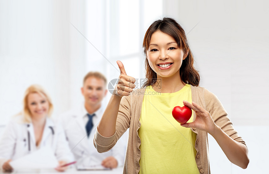 医学,医疗心脏病学的快乐的亚洲轻妇女抱着红色的玩具心脏,医院背景下医生竖大拇指快乐的亚洲女人红心竖大拇指图片