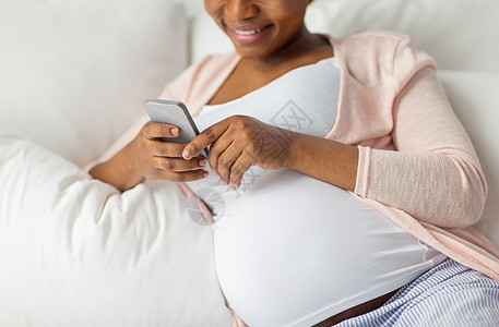 怀孕,人技术密切怀孕的非裔美国妇女与智能手机床上家家里智能手机的孕妇躺床上图片