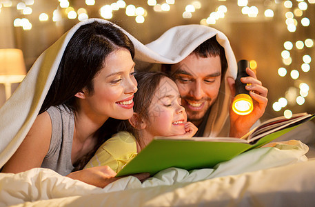 人们家庭的快乐的母亲,父亲小女儿床上阅读书,晚上躺家里的毯子下快乐的家庭阅读书晚上床上家图片