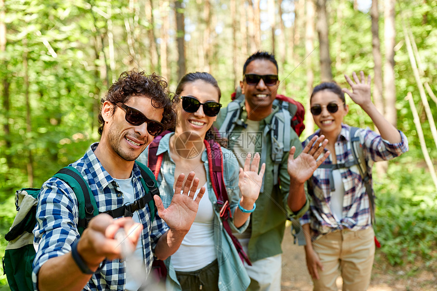 旅行,旅游,徒步旅行人的群朋友带着背包森林里用自拍棒挥手拍照朋友们带着背包徒步旅行自拍图片