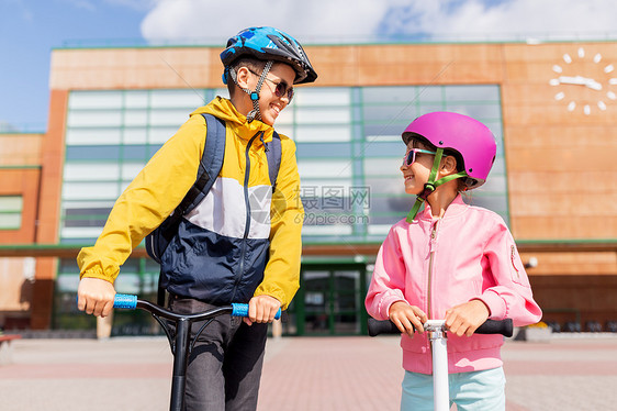 教育,童人的快乐的学校孩子戴着头盔,背包骑着滑板车户外快乐的学校孩子戴着头盔骑滑板车图片