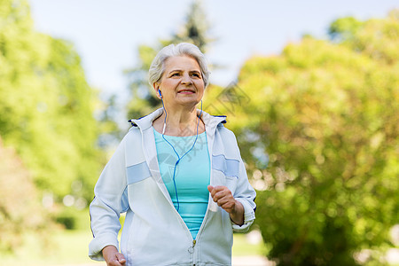 健身,运动健康的生活方式老妇女与耳机运行夏季公园戴着耳机夏天公园跑步的高级女人背景图片