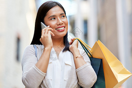 销售,消费主义人的轻的亚洲妇女,带着购物袋,城市街道上打电话给智能手机购物袋的女人打电话给智能手机图片