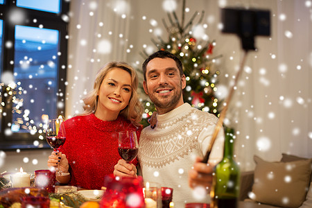 诞节,假日,技术人的快乐的夫妇雪上的家庭晚餐上自拍棒拍照夫妇诞节用自拍杆拍照图片