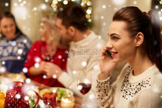 假期,沟通庆祝轻妇女打电话智能手机诞节晚餐与朋友家里下雪诞节晚餐时打电话给智能手机的女人图片