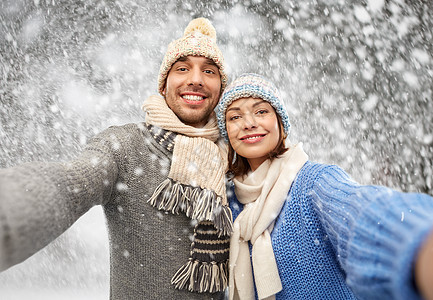 人们,诞节冬天的衣服幸福的夫妇戴着针帽围巾雪地背景上自拍穿着冬天衣服的快乐夫妇自拍图片