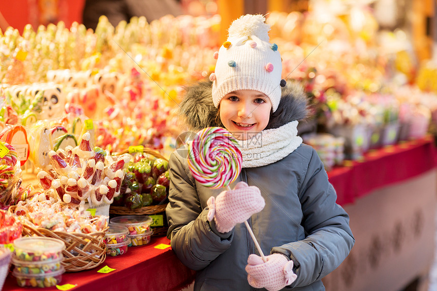 假期,童人的快乐的小女孩与大棒棒糖诞节市场糖果店晚上诞节市场糖果店里棒棒糖的女孩图片