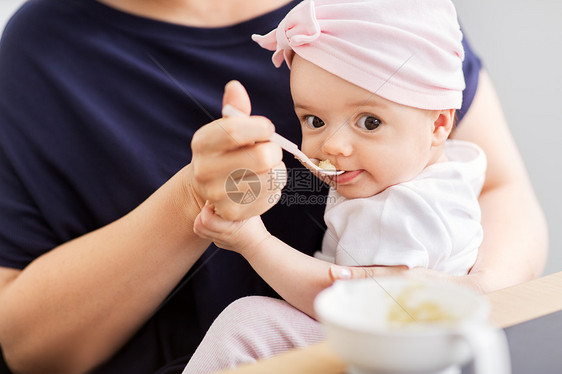 婴儿期,母亲食物的快乐的中母亲勺子喂养婴儿的女儿与纯净家里中母亲家喂婴儿女儿图片