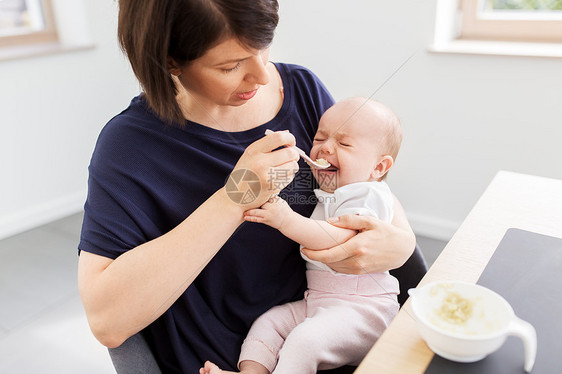 婴儿期,母亲食物的中母亲用勺子哭泣的婴儿女儿与纯净家里中母亲家喂婴儿女儿图片