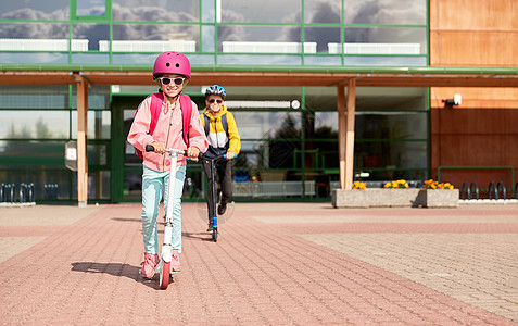 教育,童人的快乐的学校孩子戴着头盔,背包骑着滑板车户外快乐的学校孩子们户外骑滑板车图片