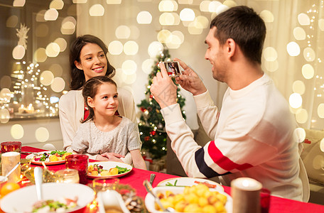 节日,家庭庆祝快乐的母亲,父亲小女儿吃诞晚餐,并家里用智能手机拍照快乐的家人诞晚餐上拍照图片