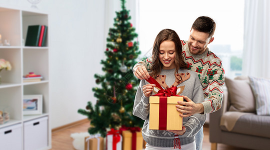 人节日的幸福夫妇的肖像与礼品盒毛衣诞树上的家庭背景诞毛衣礼品盒的幸福夫妇图片