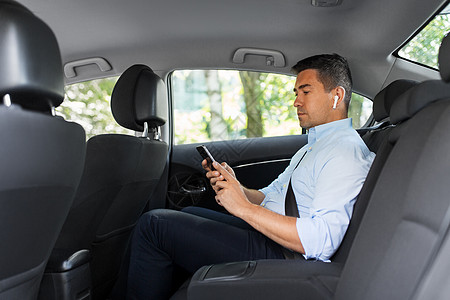 运输,商业技术男乘客商人用无线耳机用智能手机出租车后座出租车上耳机手机的乘客图片