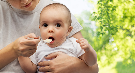 孩子,饮食食物的母亲用勺子喂养小婴儿绿色的自然背景用勺子喂小宝宝来亲近妈妈背景图片